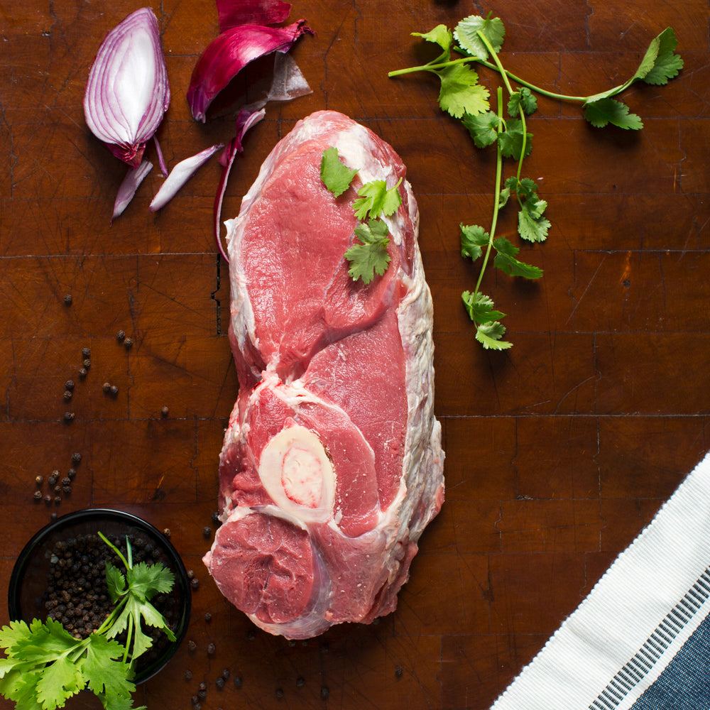 Bone-in Kentucky grass-fed Rose Veal chuck roast displayed with fresh cilantro, peppercorns, and red onion, ideal for braising or slow roasting.