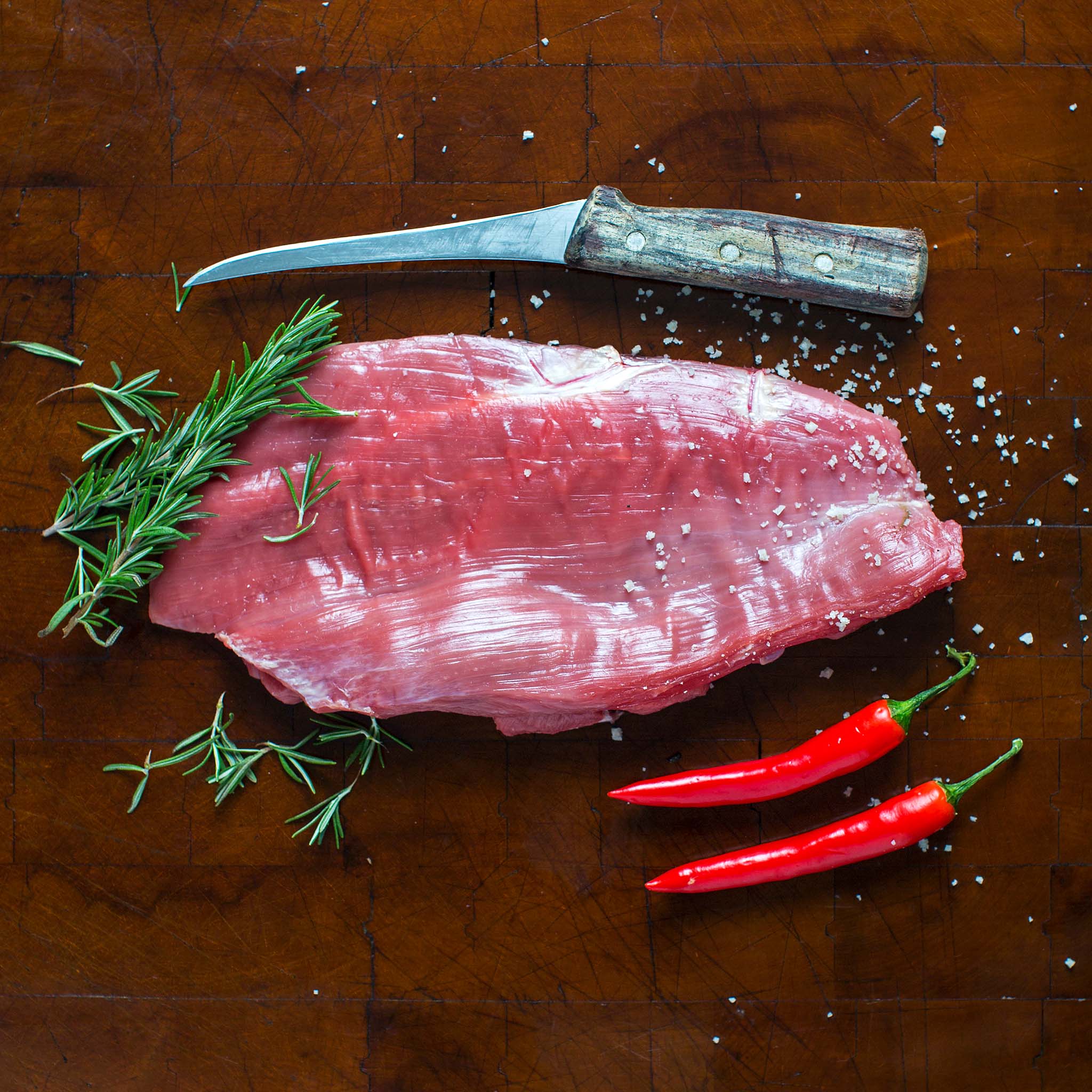 Raw Berry Beef flank steak with rosemary, chili peppers, and sea salt on a butcher’s board, Kentucky-raised beef.
