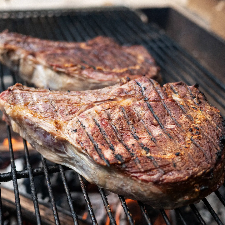Kentucky grass-fed Rose Veal ribeye steaks sizzling on a grill with perfect sear marks, ideal for summer cookouts and steak lovers.