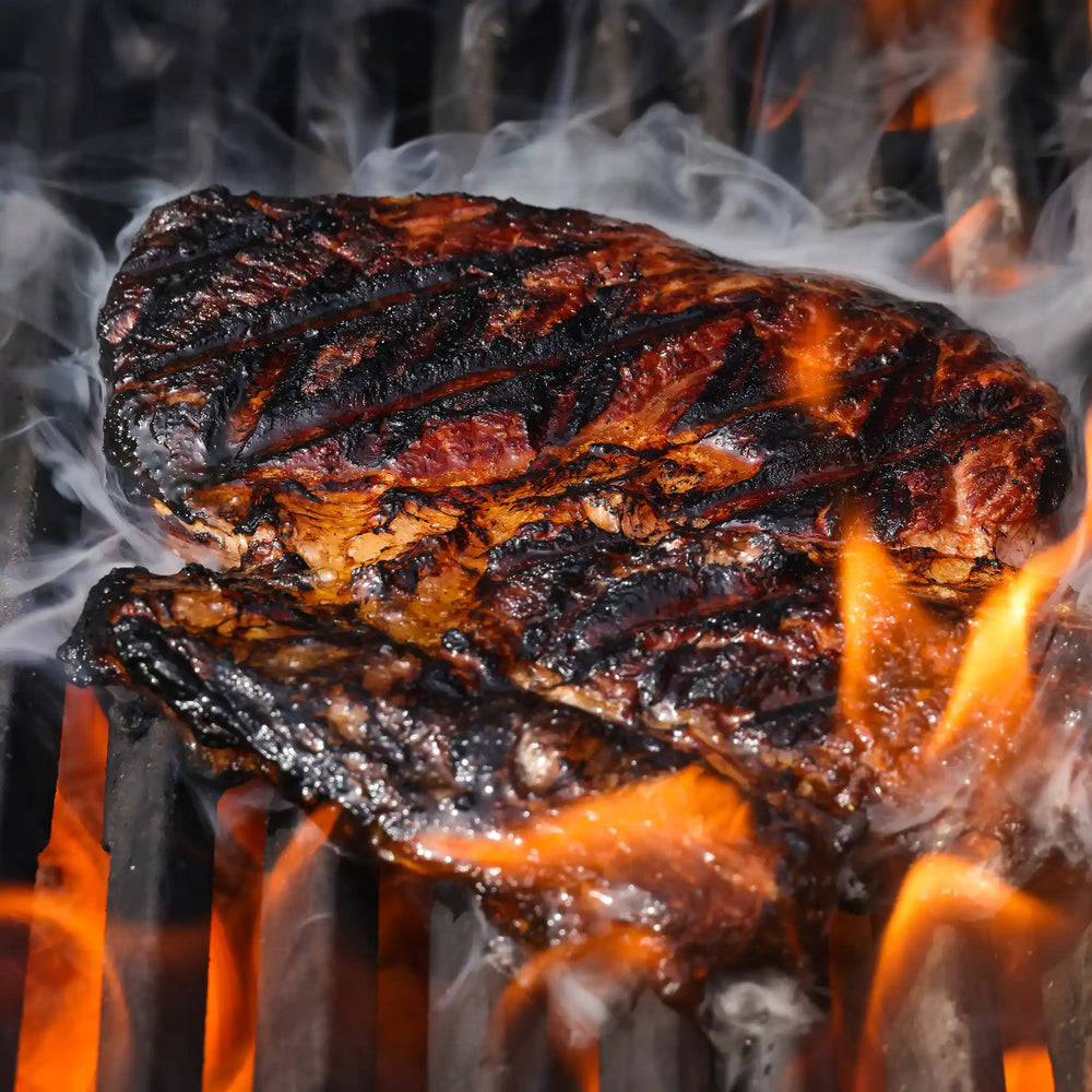 Berry Beef boneless ribeye steak grilling over open flame with charred sear marks